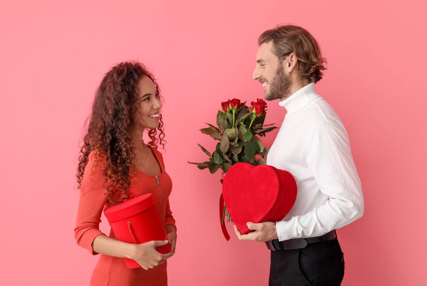 色の背景に贈り物や花を持つ幸せな若いカップル。バレンタインデーのお祝い - 写真・画像