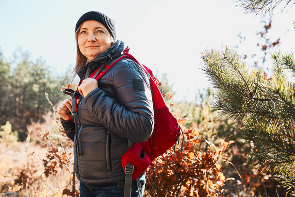 Güneşli bir tatil gününde yürüyüşe çıkan mutlu kadın. Sırt çantalı bir kadın ormanda yürüyor. Yaz tatilini doğaya yakın geçirmek - Fotoğraf, Görsel