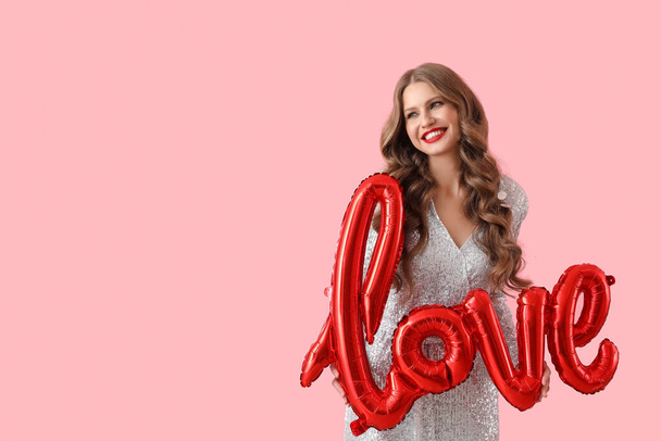 Krásná šťastná mladá žena s balónem ve tvaru slova LOVE na růžovém pozadí. Valentýnská oslava - Fotografie, Obrázek