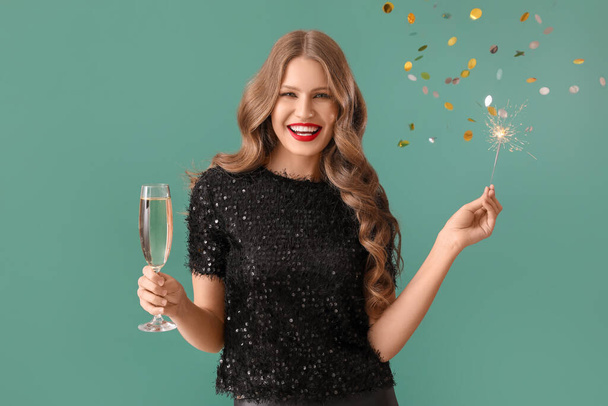 Beautiful young woman with Christmas sparkler and champagne on green background - Photo, Image