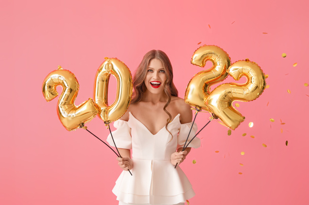 Mooie jonge vrouw met ballonnen in de vorm van figuur 2022 op roze achtergrond. Nieuwjaarsviering - Foto, afbeelding