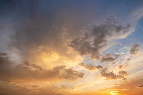 Dramatyczny zachód słońca obraz krajobrazu z bufiastymi chmurami oświetlone przez pomarańczowe zachodzące słońce i błękitne niebo - Zdjęcie, obraz