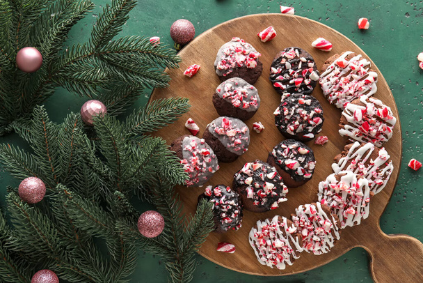 緑の背景においしいお菓子の杖クッキー、モミの枝とクリスマスボールと木製のボード - 写真・画像