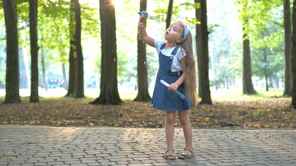 Happy little child girl blowing soap bubbles outside in green park. Outdoor summer activities for children concept - Фото, изображение