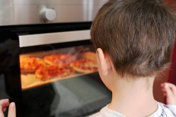 Pizza cocida en el horno y un niño observándola, primer plano de una pizza caliente con salchicha de queso, - Foto, Imagen