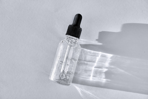 Διαφανές γυάλινο μπουκάλι σταγονόμετρο με φυσαλίδες αέρα σε γκρι φόντο. Πιπέτα με υγρό υαλουρονικό οξύ - Φωτογραφία, εικόνα