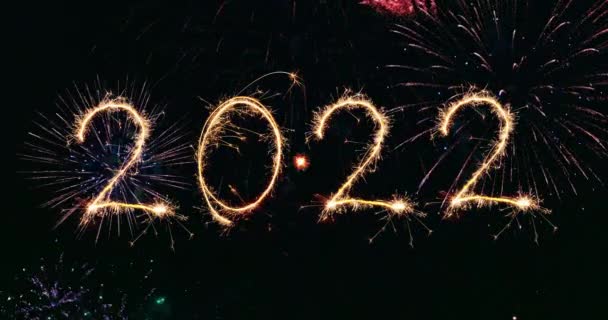 Hyvää uutta vuotta 2022 kirjoitettu Sparkle ilotulitus taivaalla ja polttava bengal valot ja ilotulitus taustalla - Materiaali, video