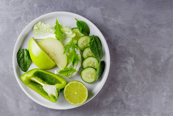 Sliced green fruits and vegetables on a gray background. Fresh green diet food in a white plate. Healthy vegetarian food concept. Copy space. Top view - Foto, immagini