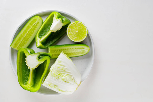 白い背景に緑の野菜や果物をみじん切り。ホワイトプレート上の緑の食事療法食品。健康的で菜食主義者。最上階だ。スペースのコピー - 写真・画像