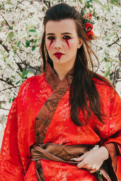 Young girl in traditional kimano in a blooming garden with samurai japanese sword katana in image of warrior woman - Valokuva, kuva