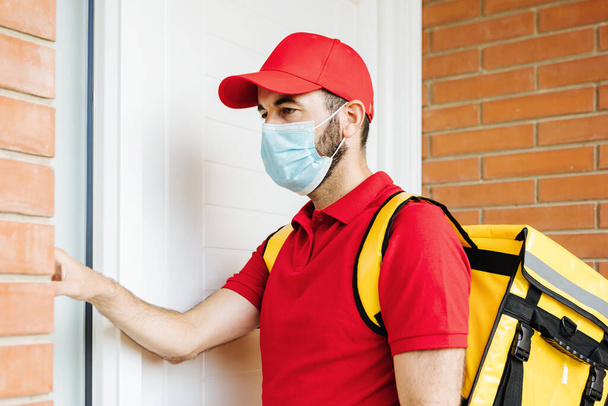 Young hispanic delivery food man in face mask ringing the doorbell - 写真・画像