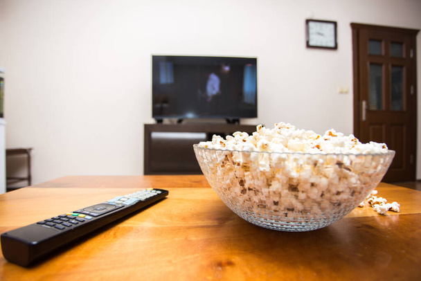 Fernbedienung und Popcorn auf einem braunen Holztisch. Konzept des Daheimbleibens in der Pandemie. - Foto, Bild