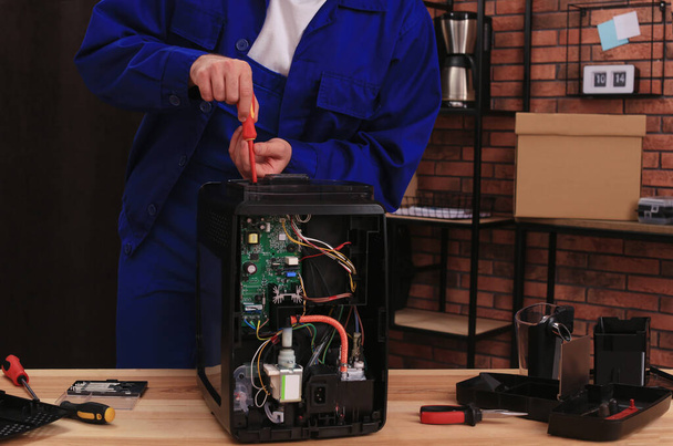 Repairman with screwdriver fixing coffee machine at table indoors, closeup - Foto, afbeelding