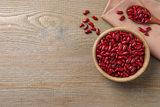 Raw red kidney beans with bowl, spoon and napkin on wooden table, flat lay. Space for text - 写真・画像