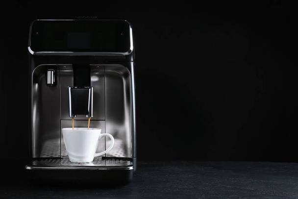 Making coffee with modern espresso machine on grey table against black background. Space for text - Foto, afbeelding