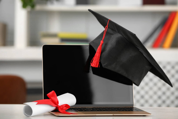 Graduation hat, student's diploma and laptop on white table indoors - Photo, image