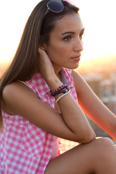 Pretty girl sitting on the roof at sunset. - Foto, imagen