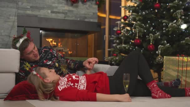 Cariñosa pareja joven tumbada junto a la chimenea bebiendo vino en Nochebuena - Imágenes, Vídeo