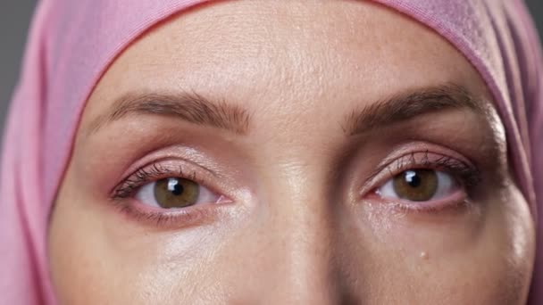Mujer joven en hijab rosa parpadea mirando a la lente de la cámara - Imágenes, Vídeo