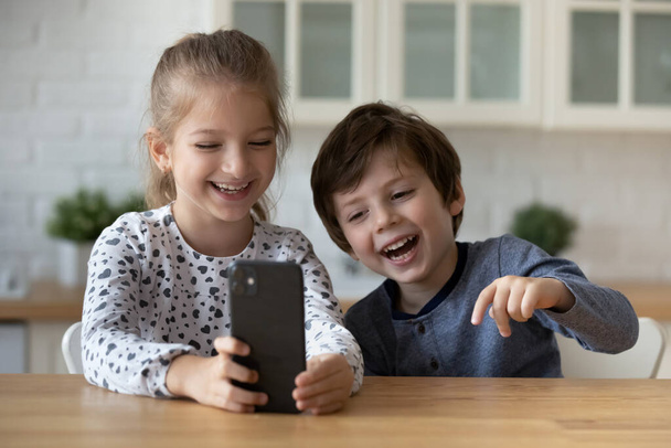 Overjoyed little sister and brother using smartphone, having fun - Photo, image