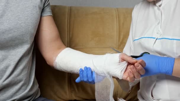 Pielęgniarka tnie bandaż gipsowy z uzdrowionego ramienia młodego człowieka - Materiał filmowy, wideo