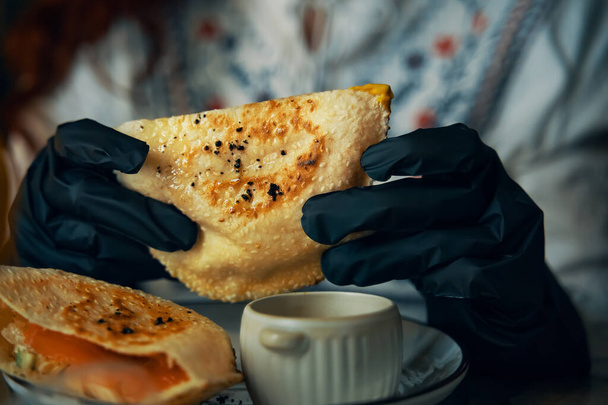 Vrouwelijke handen in zwarte handschoenen houden traditionele pitas sandwich. - Foto, afbeelding