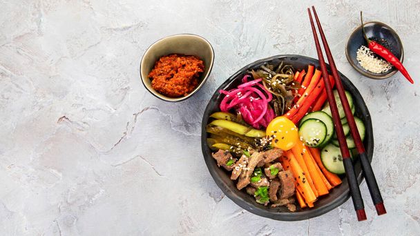 Bibimbap con snacks sobre fondo gris. Comida tradicional coreana. Vista superior, plano, espacio para copiar - Foto, Imagen
