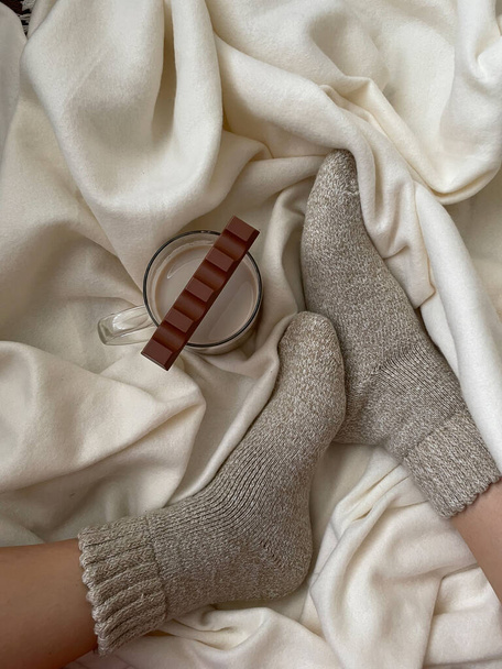 Atmospheric photo. The girl's feet are in wool socks with a mug of cocoa and milk chocolate. Vertical photo. - Photo, image