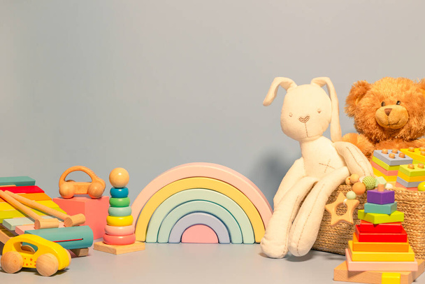 Toys background. Toy box with teddy bear, bunny and wood rattle. Educational wooden Montessori toys on pastel blue background. Cute toys collection for small children. Front view - Photo, Image