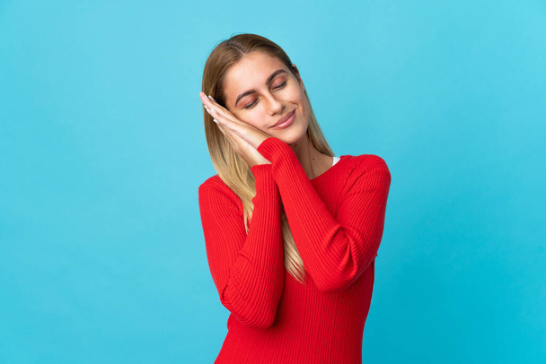 Young blonde woman isolated on blue background making sleep gesture in dorable expression - Photo, Image