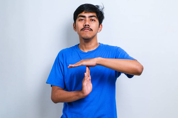 Jonge knappe man draagt casual shirt staan over witte achtergrond Doen time-out gebaar met handen, gefrustreerd en serieus gezicht - Foto, afbeelding