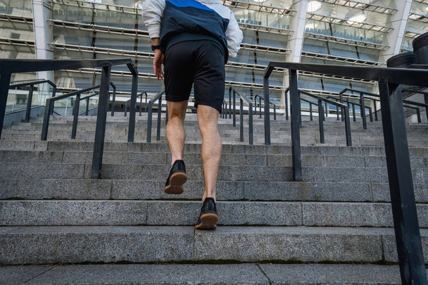 Sport exercise and healthy lifestyle concept. Low angle, cropped view of sportsman running on steps, training outdoors, warm up his body, getting ready to daily workout in the city, back rear shot - Fotoğraf, Görsel