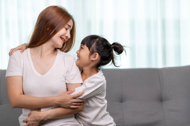 Menschen und Familienkonzept - glücklich lächelndes Mädchen mit Mutter, die sich zu Hause auf dem Sofa umarmt - Foto, Bild