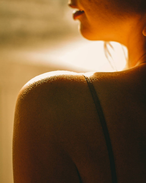 A vertical closeup shot of the sun shining on a delicate female's shoulder - Fotoğraf, Görsel