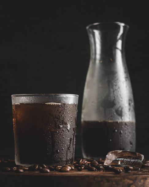A vertical closeup of a glass of cold coffee with a bottle in the background. - Foto, Bild