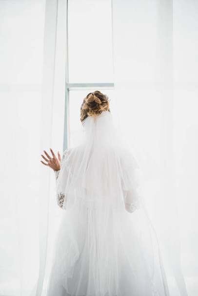 a beautiful bride in a magnificent dress throws the curtains - Фото, зображення