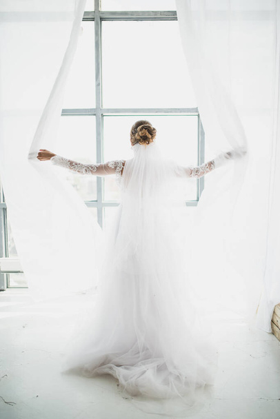 a beautiful bride in a magnificent dress throws the curtains - Фото, изображение