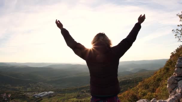 Jong meisje stak haar handen op naar de zon tegen de achtergrond van de bergen, slow motion - Video