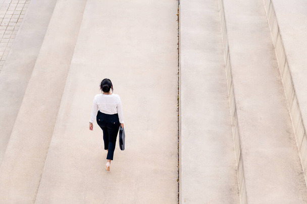 top view of an unrecognizable businesswoman walking with a briefcase on a concrete floor, concept of successful entrepreneur and urban lifestyle, copy space for text - Fotografie, Obrázek