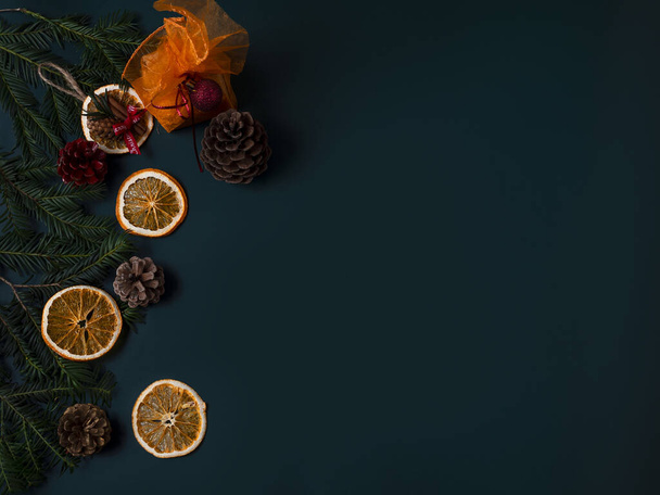 A top view of pine branches and cones with dried orange slices on a dark surface with space for text - Fotó, kép