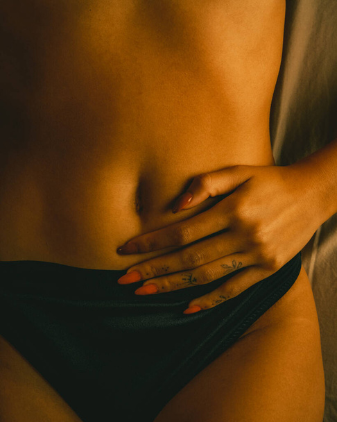 A vertical shot of a female hand on her delicate bare stomach area - Foto, imagen