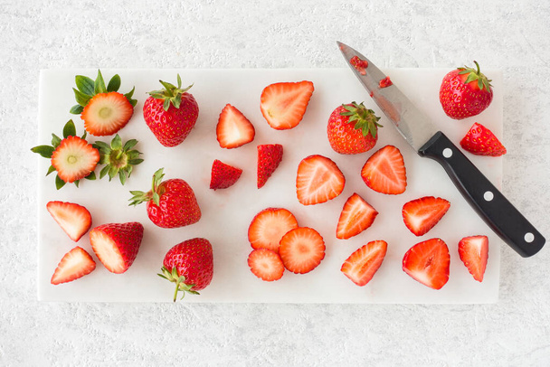 Closeup of cut and whole strawberries on white marble cutting board with knife. Top view.  - Fotografie, Obrázek