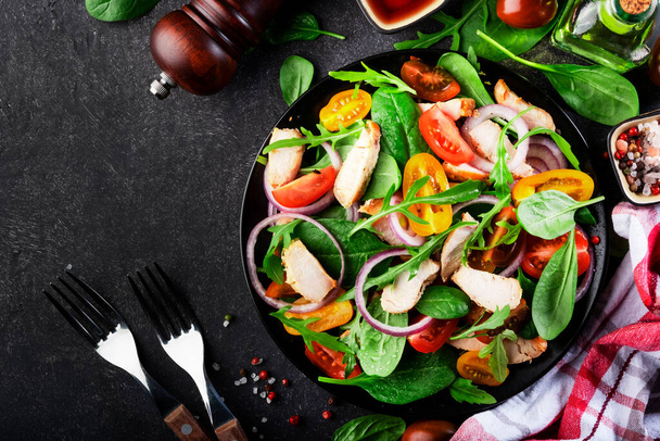Gezonde salade met spinazie, gegrilde kip, tomaten, arugula en rode ui. Zwarte tafel, kopieerruimte - Foto, afbeelding