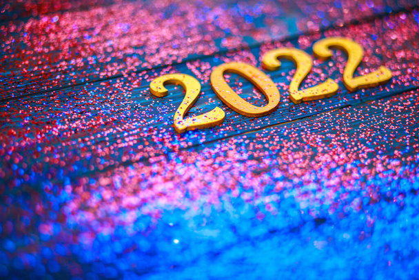 2022 new year, golden numbers on a blue wooden background, many bright sparkles, special blur, focus on numbers, festive background, sparkling tinsel, new year date. - Foto, Imagem