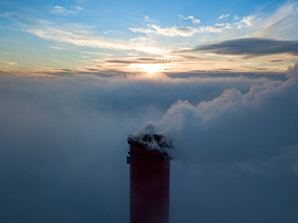 Wysoki komin elektrowni cieplnej nad mgłą w promieniach zachodu słońca. Widok drona z powietrza. - Zdjęcie, obraz