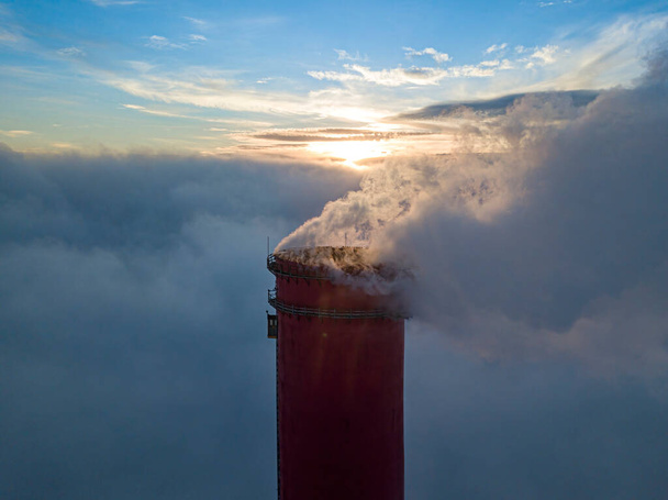 Hoher Schornstein eines Wärmekraftwerks über dem Nebel im Sonnenuntergang. Drohnenblick aus der Luft. - Foto, Bild
