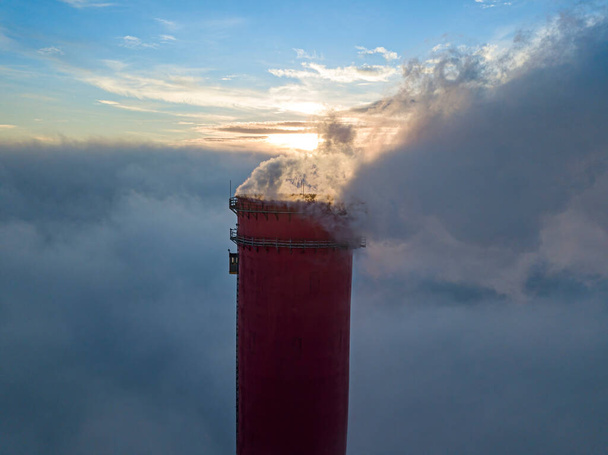 Высокий дымоход тепловой электростанции над туманом в лучах заката. Воздушный беспилотник. - Фото, изображение