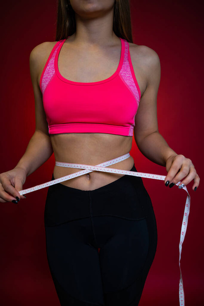 Slim tanned woman's body in sports wear over pink background - Photo, Image
