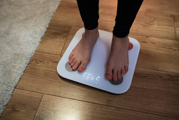Een gezonde vrouw die op een weegschaal staat om haar gewicht in de woonkamer te meten. Hormonen, gewichtsverlies, ideaal gezond gewicht, Metabolisme, Dieet. - Foto, afbeelding