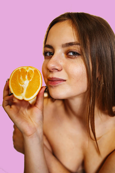Βιταμίνη C για το δέρμα. Ενθουσιασμένη νεαρή όμορφη γυναίκα με κλειστά μάτια κρατώντας πορτοκαλί μισό πάνω από ροζ φόντο - Φωτογραφία, εικόνα